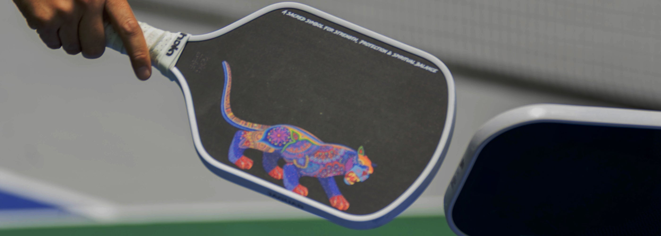 Hola Jaguar paddle with colorful jaguar design held by a hand